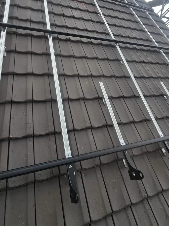 Ziegeldach von unten fotografiert: quer darüber zwei schwarze Schneefang-Rohre, das untere auf zwei geschwungenen Haltern verschraubt, längs dazu die hellen Montageschienen für die Solarmodule