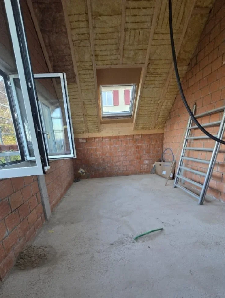 Dachgeschoss im Rohbau von innen: zwischen den Sparren der Schräge liegt die Dämmung, die Wände sind noch Backstein, das Dachfenster ist eingesetzt