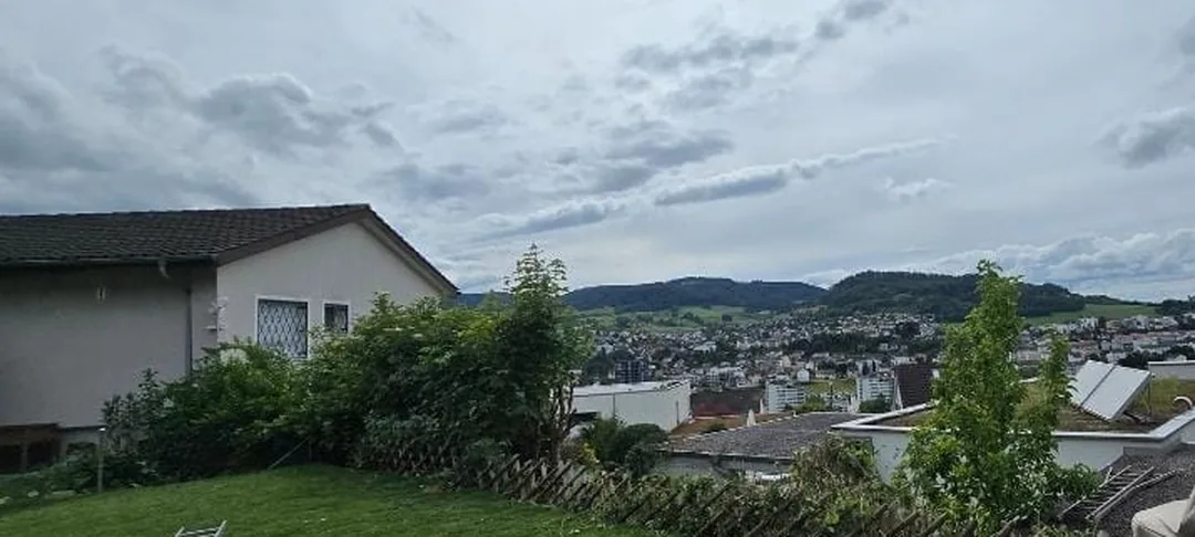 Derselbe Garten nach der Arbeit, dasselbe Haus links im Bild: die hohen Sträucher sind entfernt, vom Rasen aus geht der Blick frei über die Dächer des Dorfes bis zu den bewaldeten Hügeln